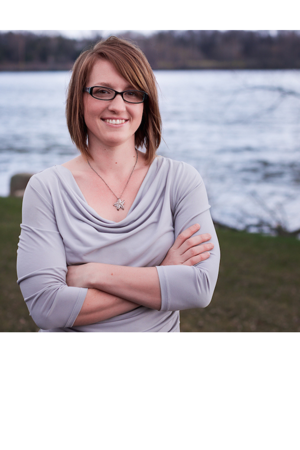 A woman with glasses and a gray top stands with her arms crossed.